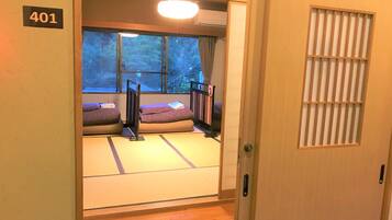 Una habitación japonesa tradicional con suelo de tatami, un futón, una puerta corredera y una ventana con vistas a árboles.