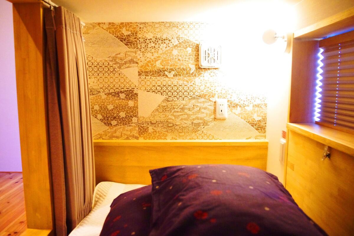 Una habitación pequeña y acogedora con cama, ventana con persianas y un diseño geométrico en la pared.