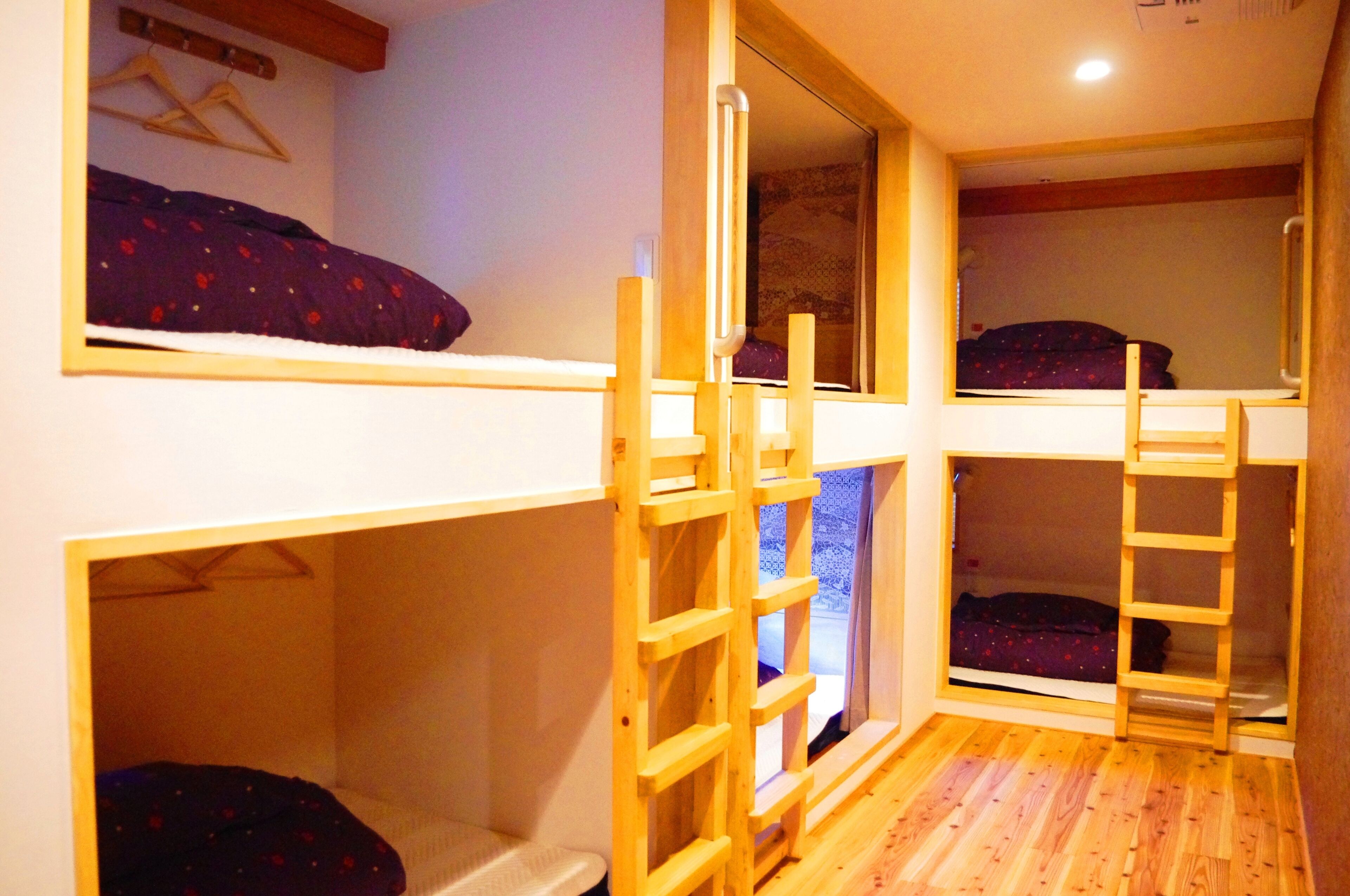A dormitory-style room with bunk beds, wooden ladders, and a window.