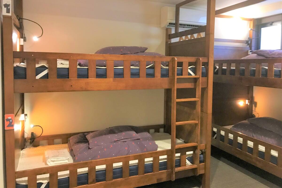 Dormitorio con literas, una escalera, aire acondicionado de pared y una mesita con lámpara.
