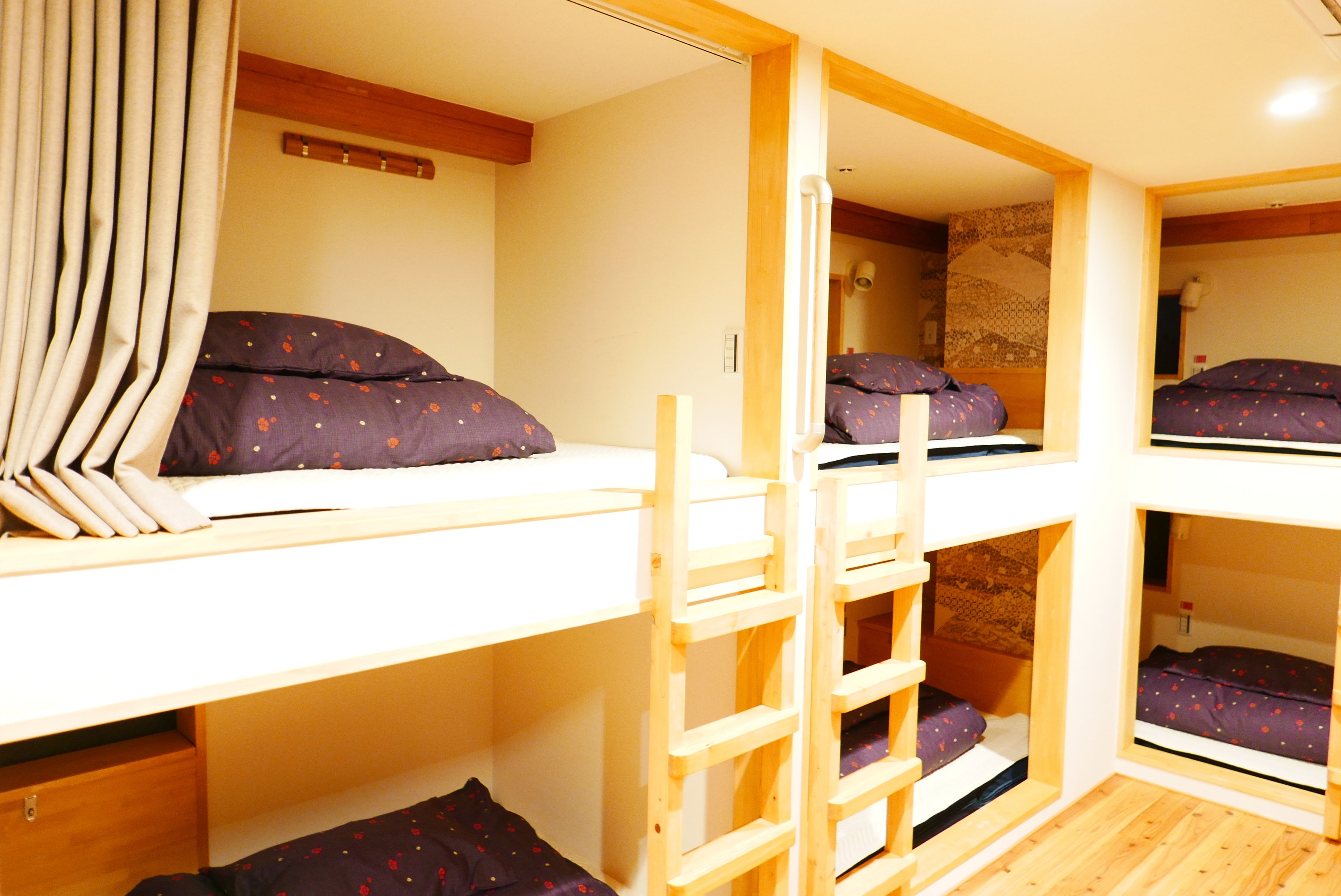 A dormitory-style room with bunk beds, wooden ladders, and a curtain.