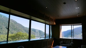 A room with large windows offering a view of a mountainous landscape. There are two chairs and a small table. - Onsen Hostel K's House Hakone (Hakone)