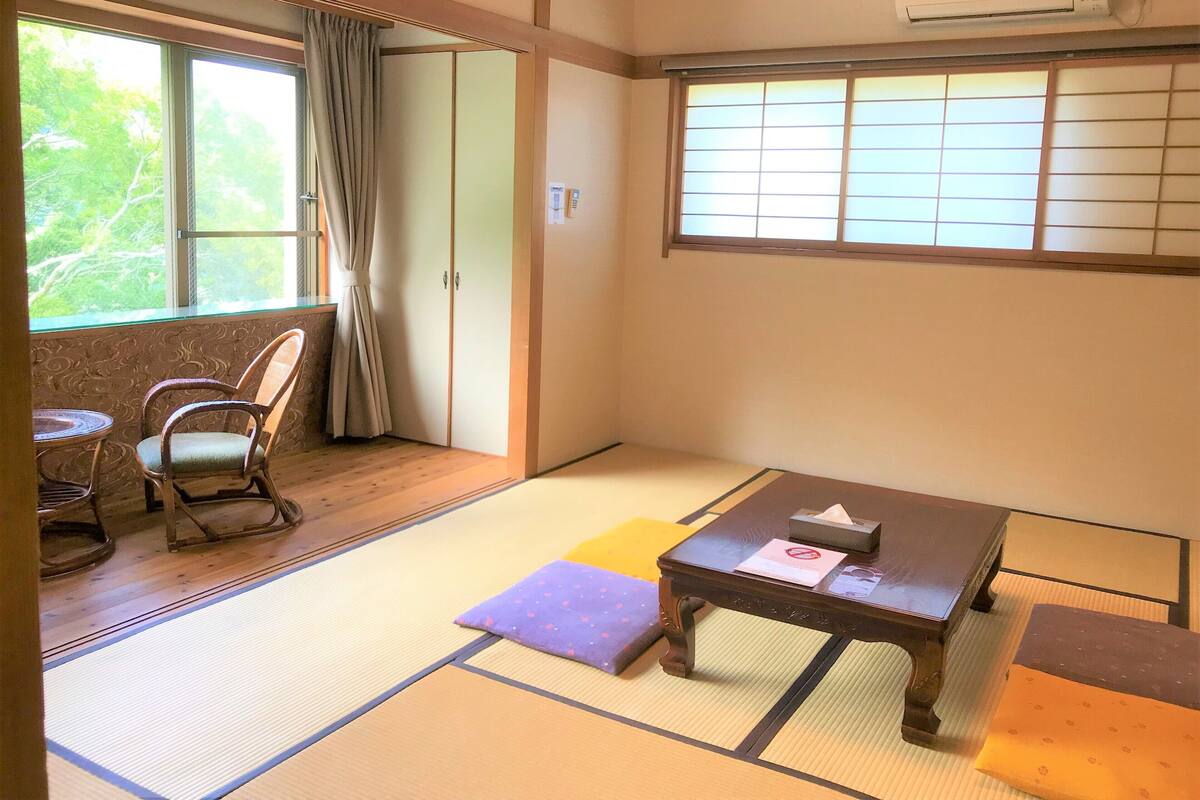 Una habitación japonesa tradicional con suelo de tatami, una mesa de madera baja, una silla y puertas correderas.