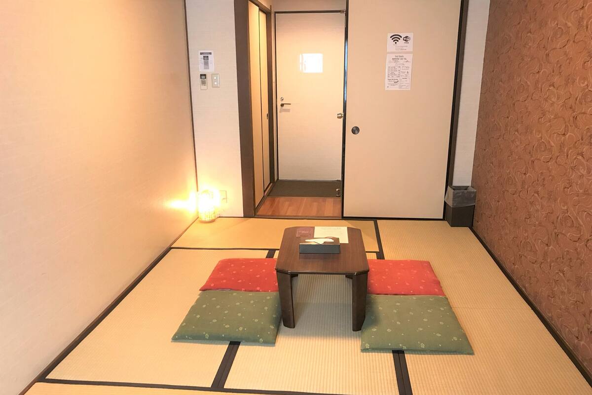 Una habitación japonesa tradicional con suelo de tatami, una mesa baja con cojines y un puertas correderas.