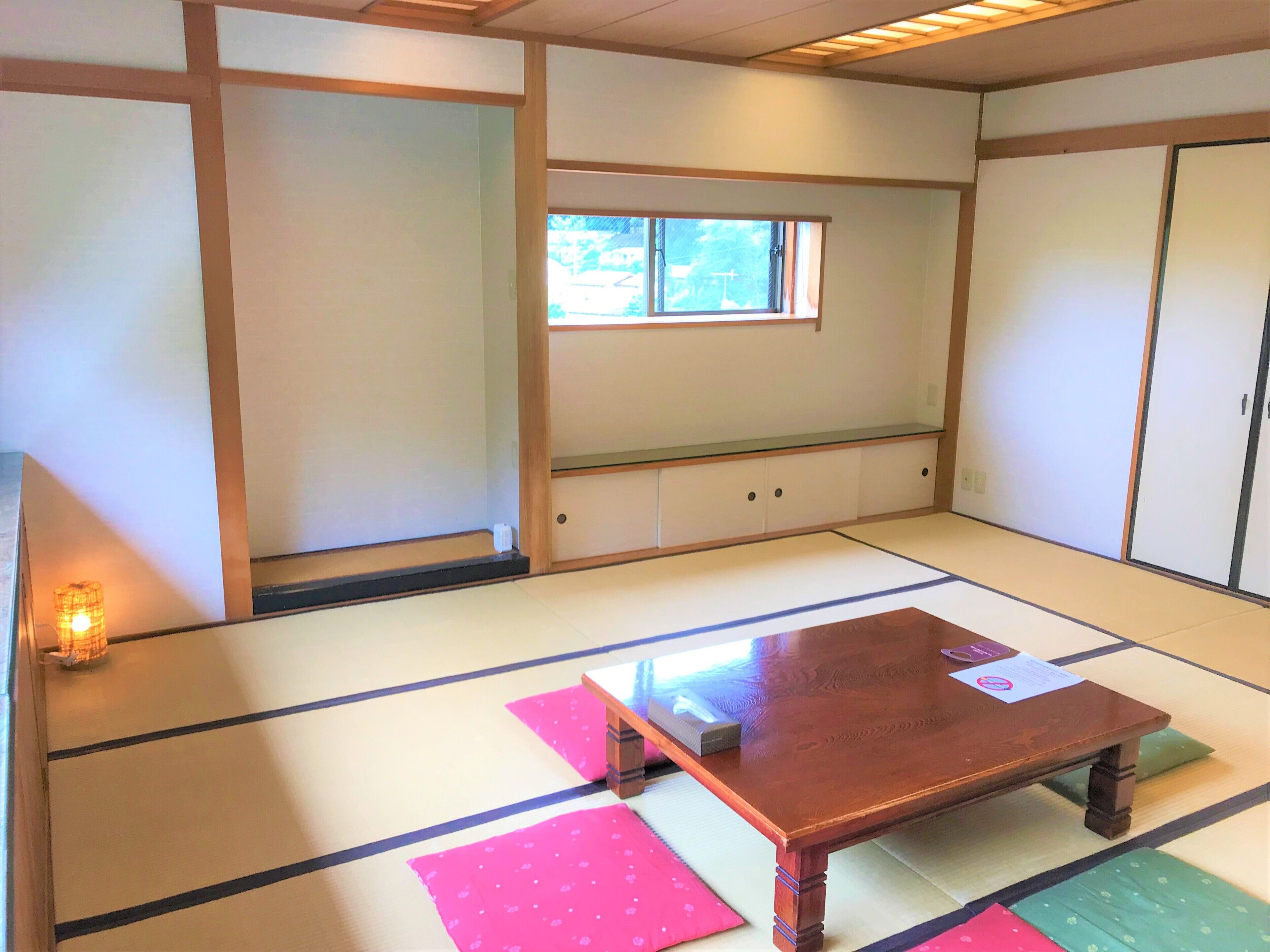 A tatami mat room with a wooden table, cushions, and a window.