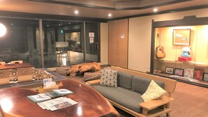 A modern living room with a wooden coffee table, grey sofa, and a small wooden side table. - Onsen Hostel K's House Hakone (Hakone)