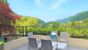 A terrace with wicker chairs and a table, overlooking a mountainous landscape with greenery and buildings. - Onsen Hostel K's House Hakone (Hakone)
