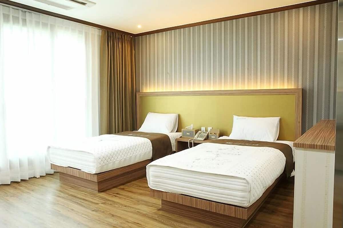 A hotel room with two beds, a bedside table with a phone, and a window with curtains.