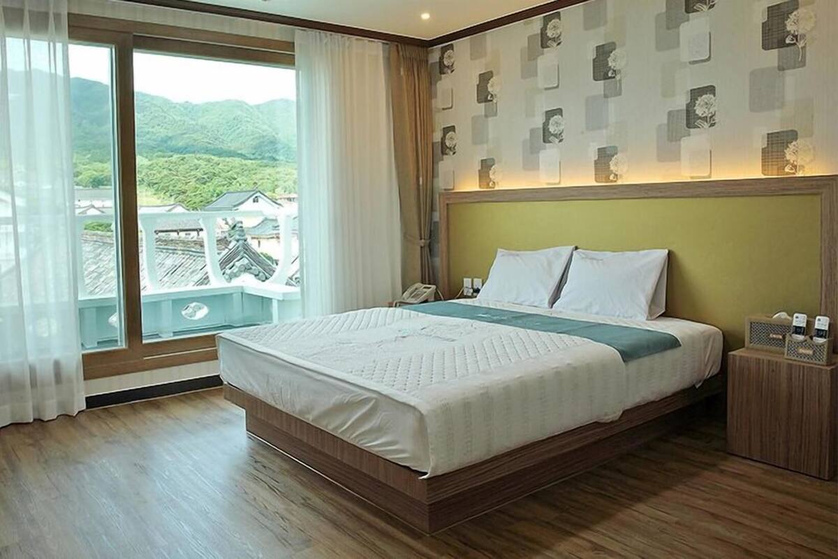 A hotel room with a large bed, a wooden floor, a balcony with a view of greenery, and a patterned wall.