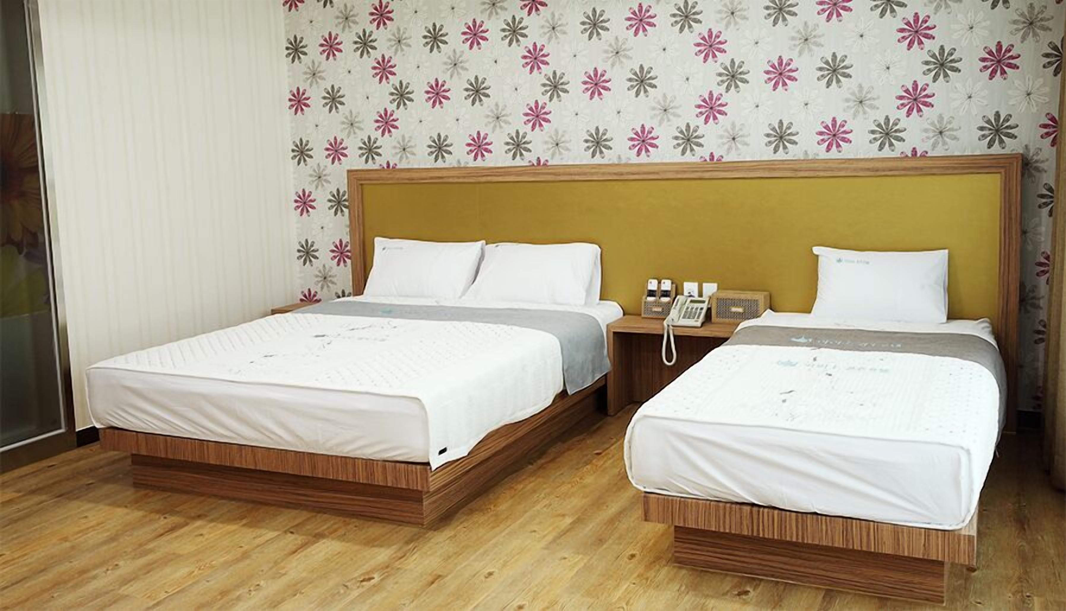 A hotel room with two beds, a wooden headboard, a telephone, and a floral wallpaper pattern.
