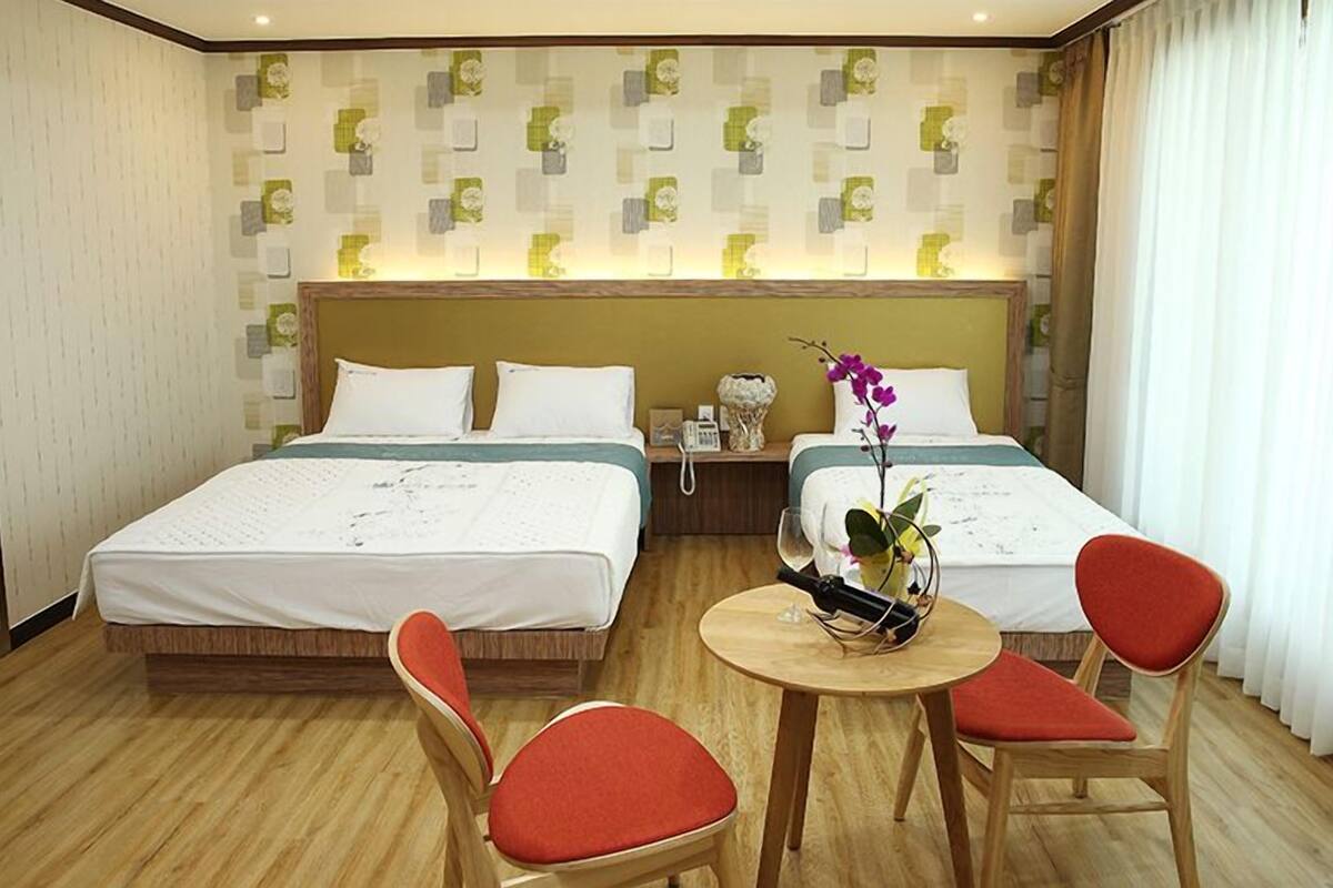 A hotel room with two beds, a round wooden table, and two red chairs.