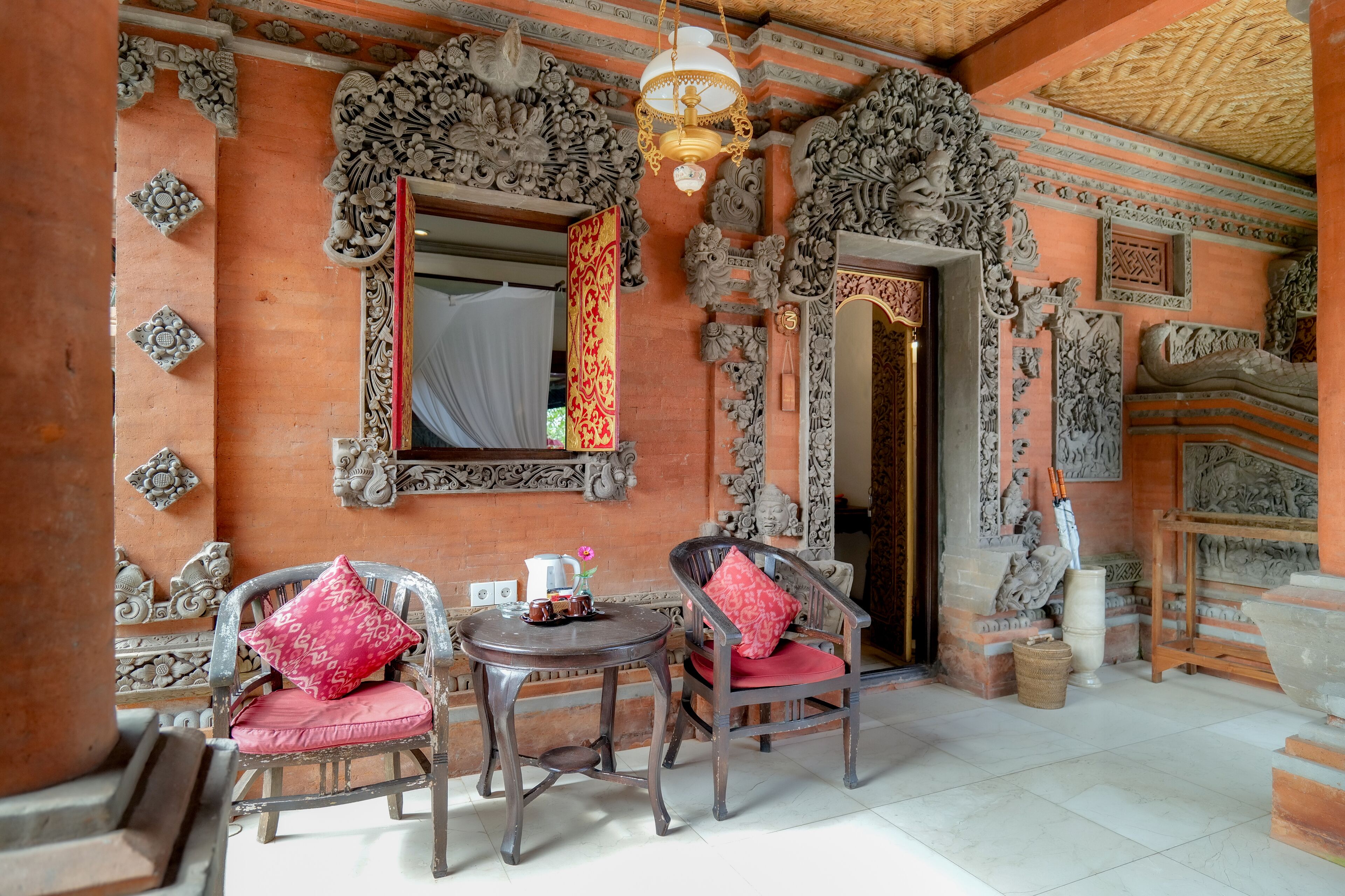 Un interior tradicional con elaboradas tallas, una cortina roja estampada y una silla de madera con cojín rojo.