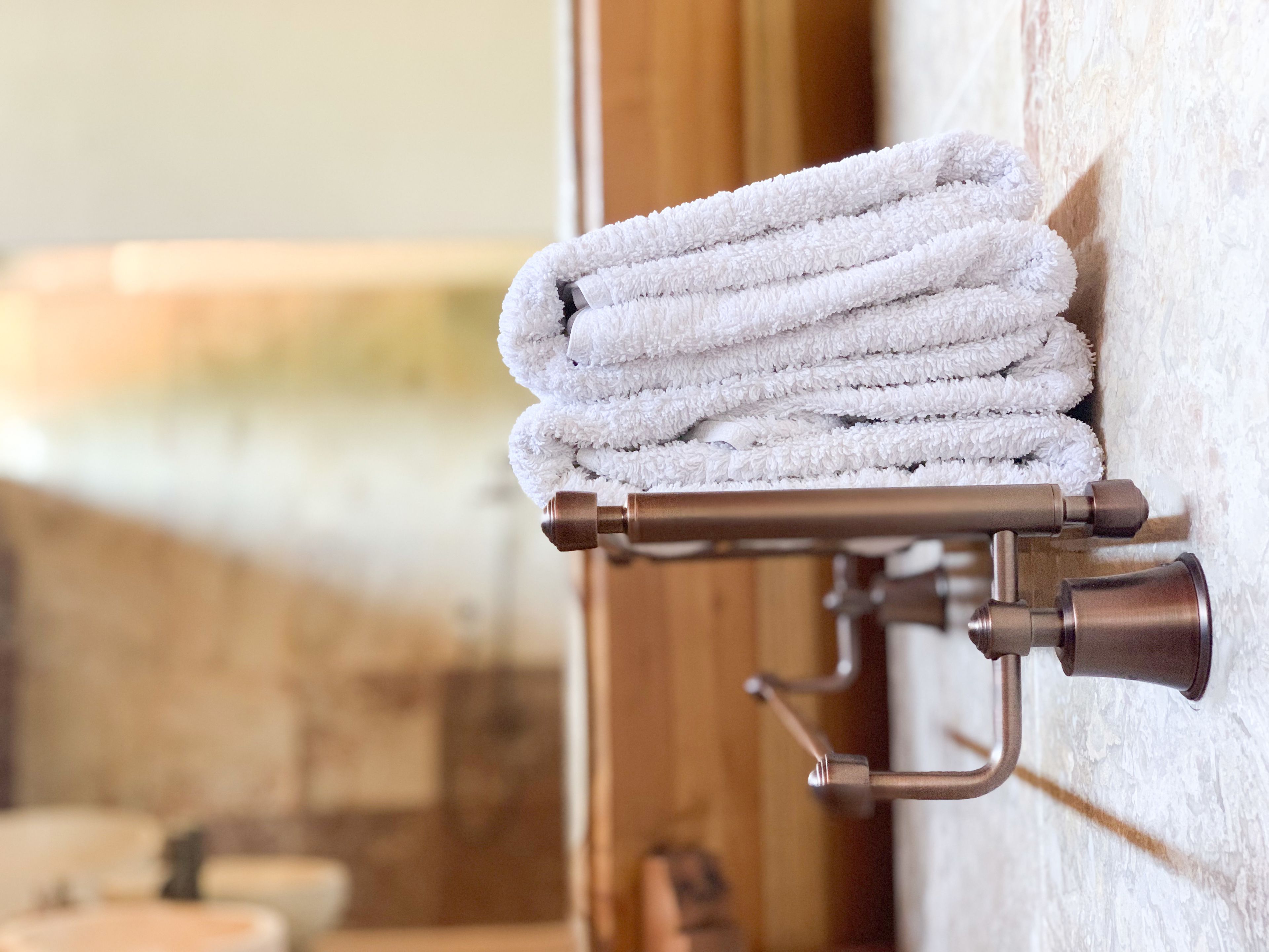 A towel rack with neatly folded towels against a textured wall.