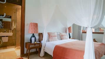 A bedroom with a four-poster bed, a bedside table with a lamp, and a view of the bathroom.