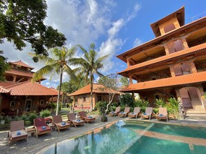 A resort with a swimming pool, lounge chairs, and traditional architecture.