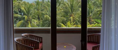 A balcony with a view of palm trees and a wooden table with chairs.