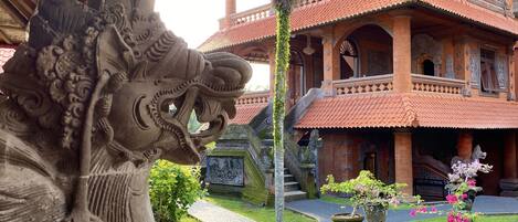 A traditional building with intricate carvings, a stone elephant sculpture, and a well-maintained garden with a pond and potted plants.