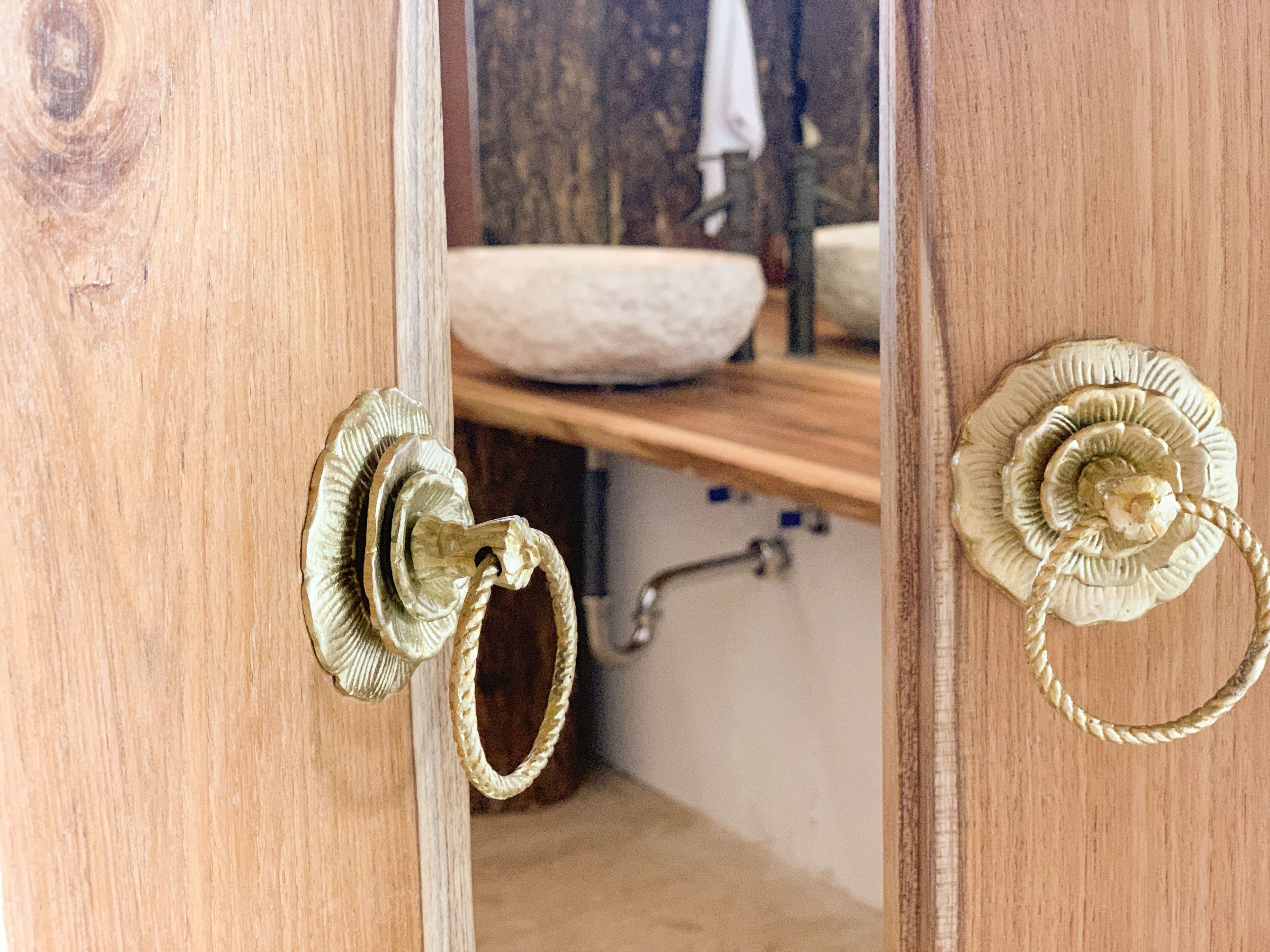 Une porte en bois ornée de poignées en laiton et d’un miroir qui reflète l’intérieur d’une salle de bain.