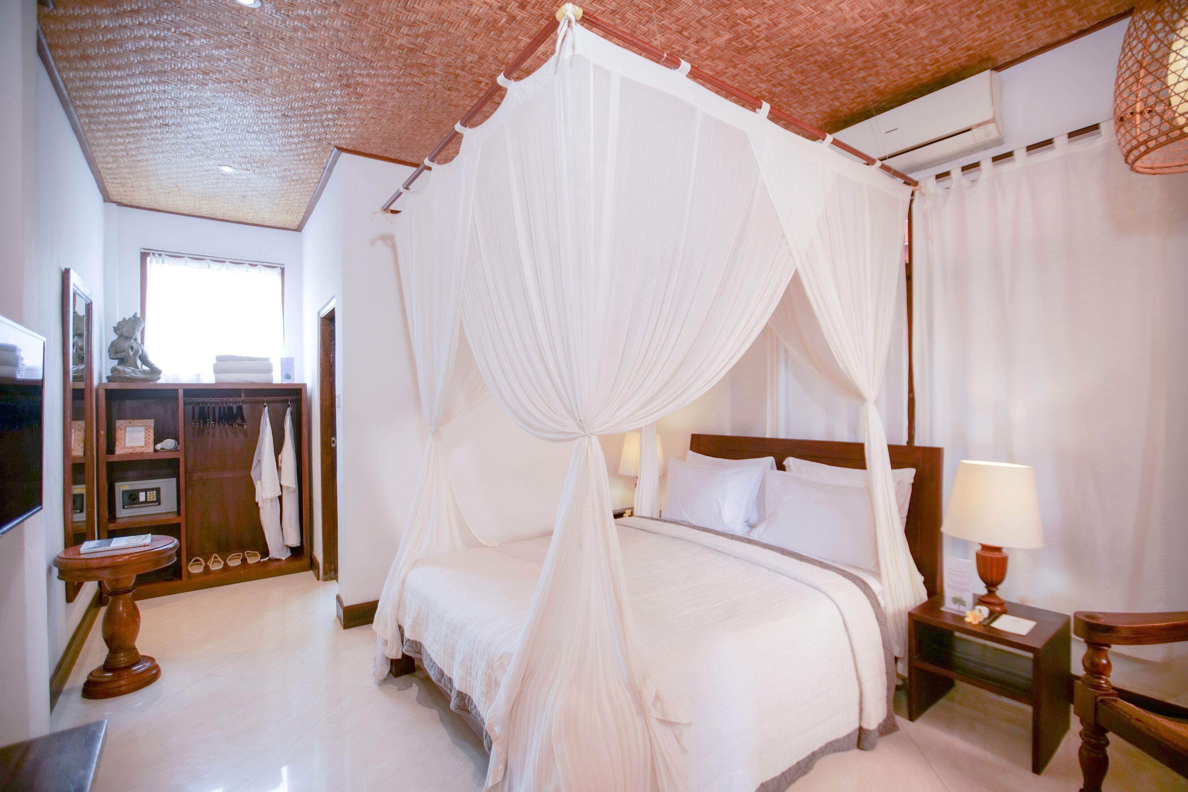 A bedroom with a four-poster bed, a bedside table with a lamp, and a wardrobe with hanging clothes.