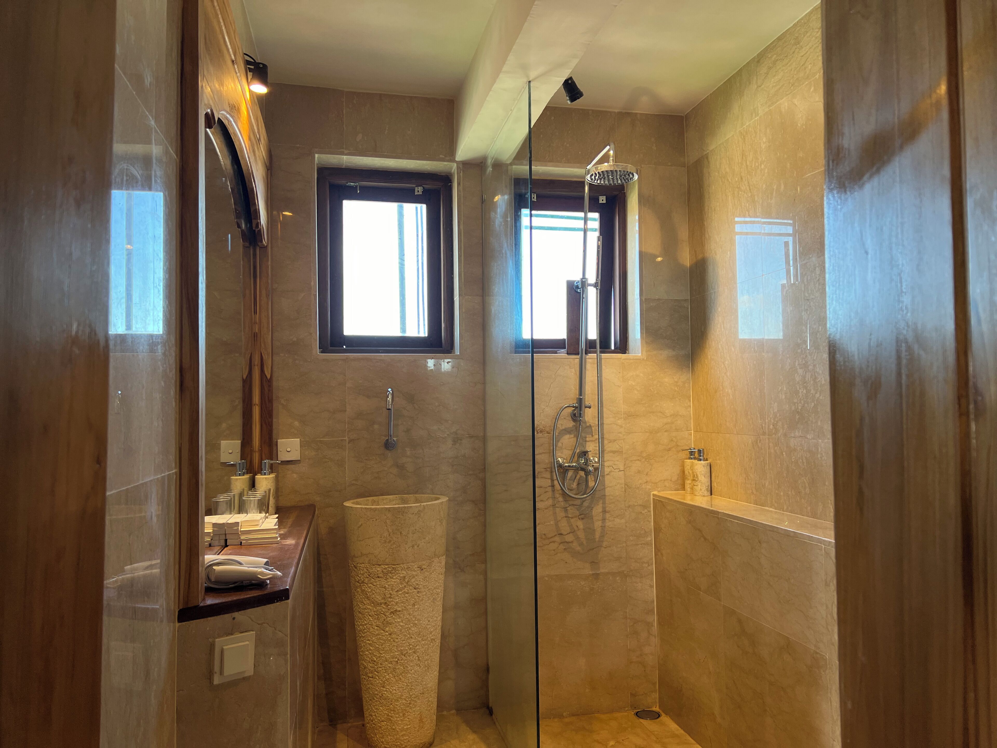 A modern bathroom with a glass-enclosed shower, a vanity with a mirror, and a window providing natural light.