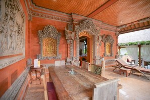 An ornate room with a large wooden table, intricate wall carvings, and a view of the outdoors.