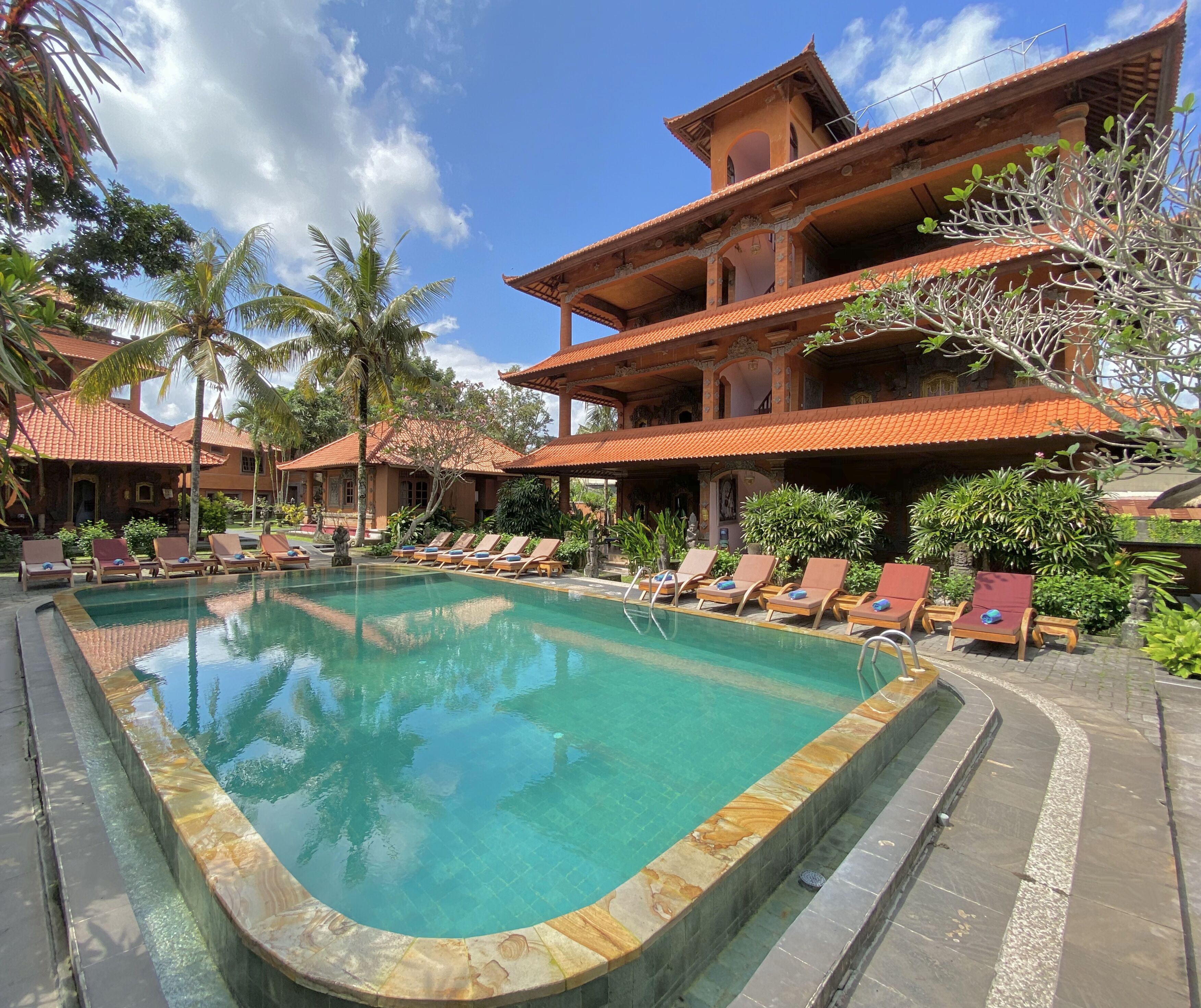 A pool area with lounge chairs and a large building with a tiled roof.