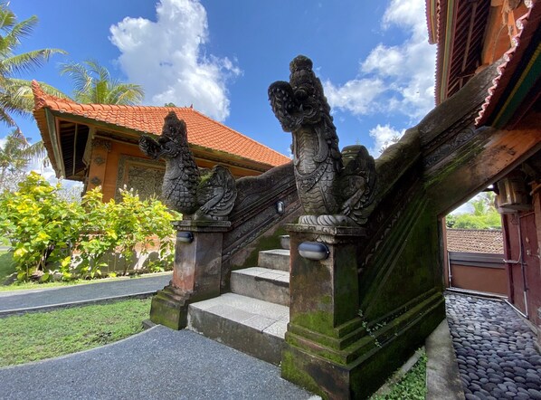 A staircase with stone lion statues at the top, leading to a building with a red-tiled roof. - Gayatri (Ubud)