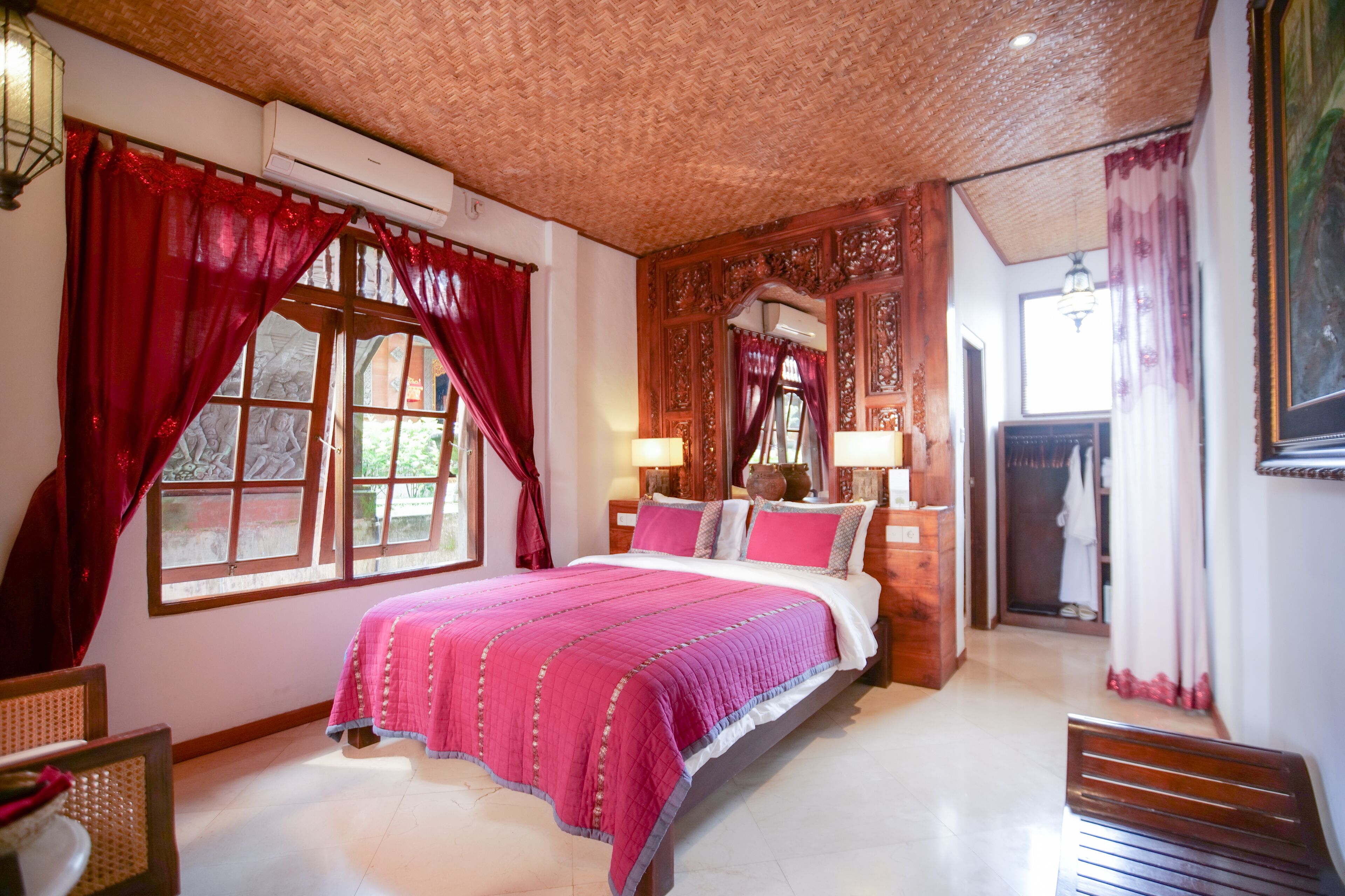 A bedroom with a large bed, red curtains, a wooden headboard, and a mirror.