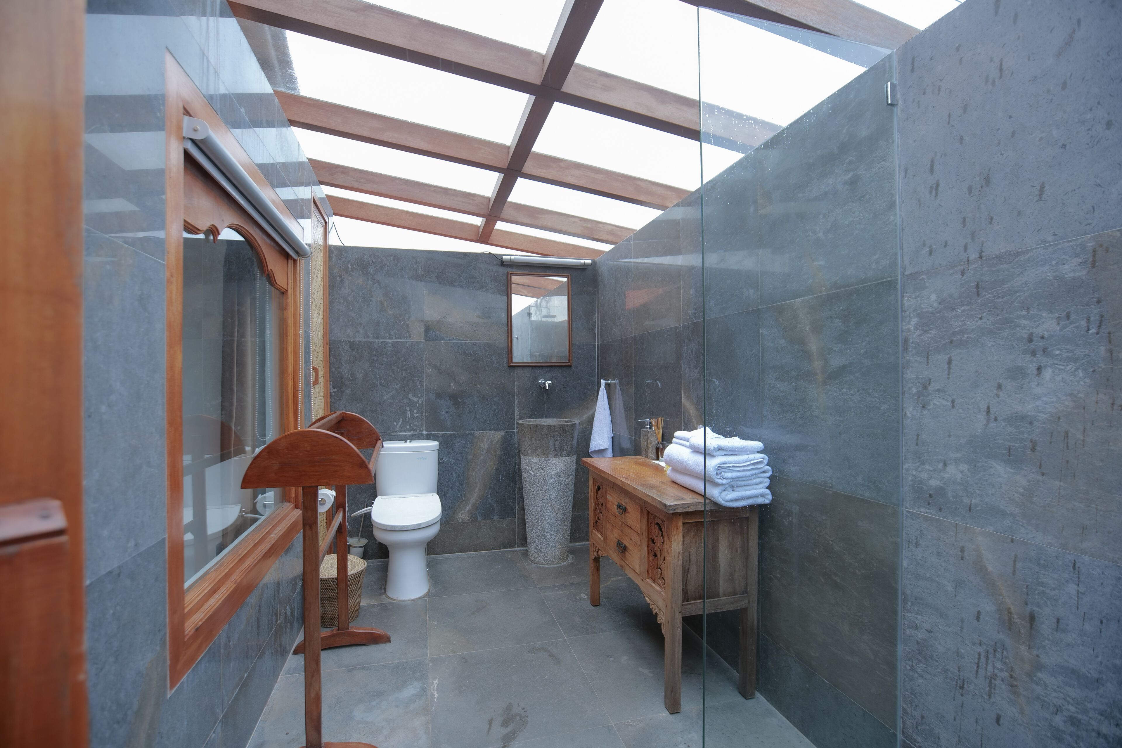 Un baño con tragaluz, tocador de madera, inodoro y lavamanos de piedra.