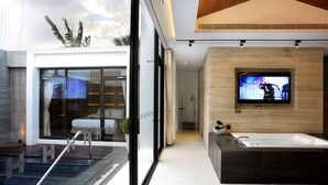 A modern bathroom with a large bathtub, a television mounted on the wall, and a view of the outside through large windows. - H Villa (Tainan)