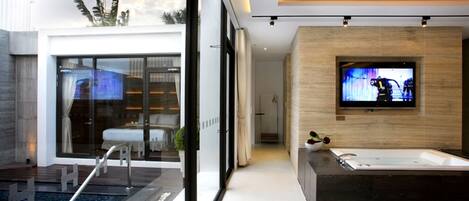 A modern bathroom with a large bathtub, a television mounted on the wall, and a view of the outside through large windows.