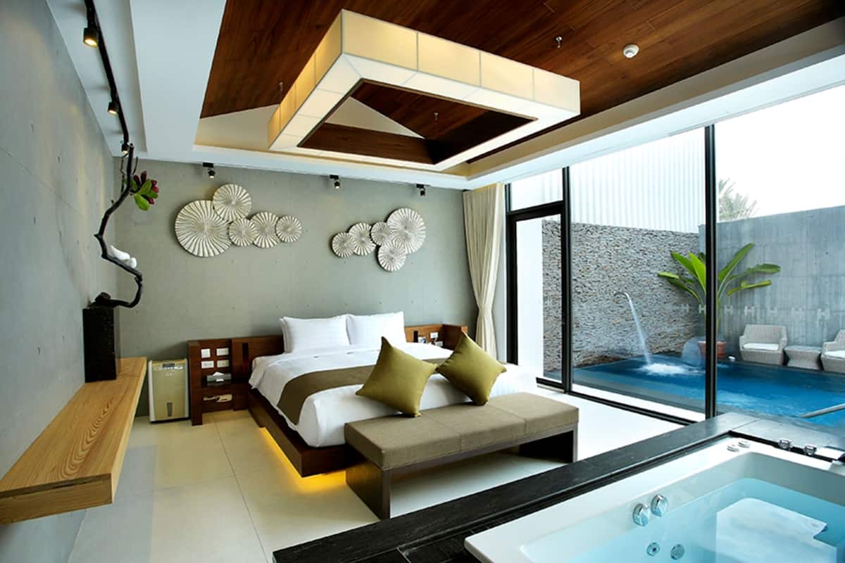 A modern bedroom with a large bed, a bench, a bathtub, and a view of a swimming pool.