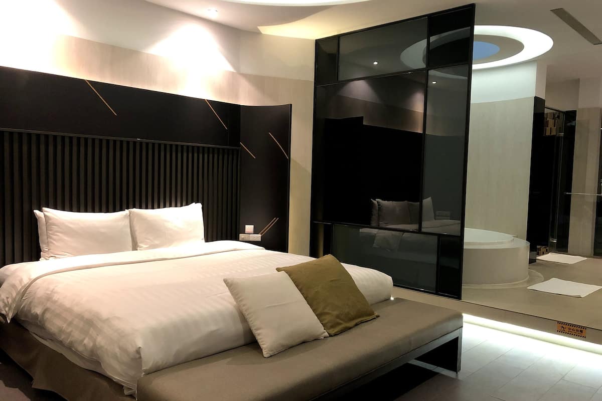 A modern bedroom with a large bed, a bedside table, a mirror, and a glass partition.