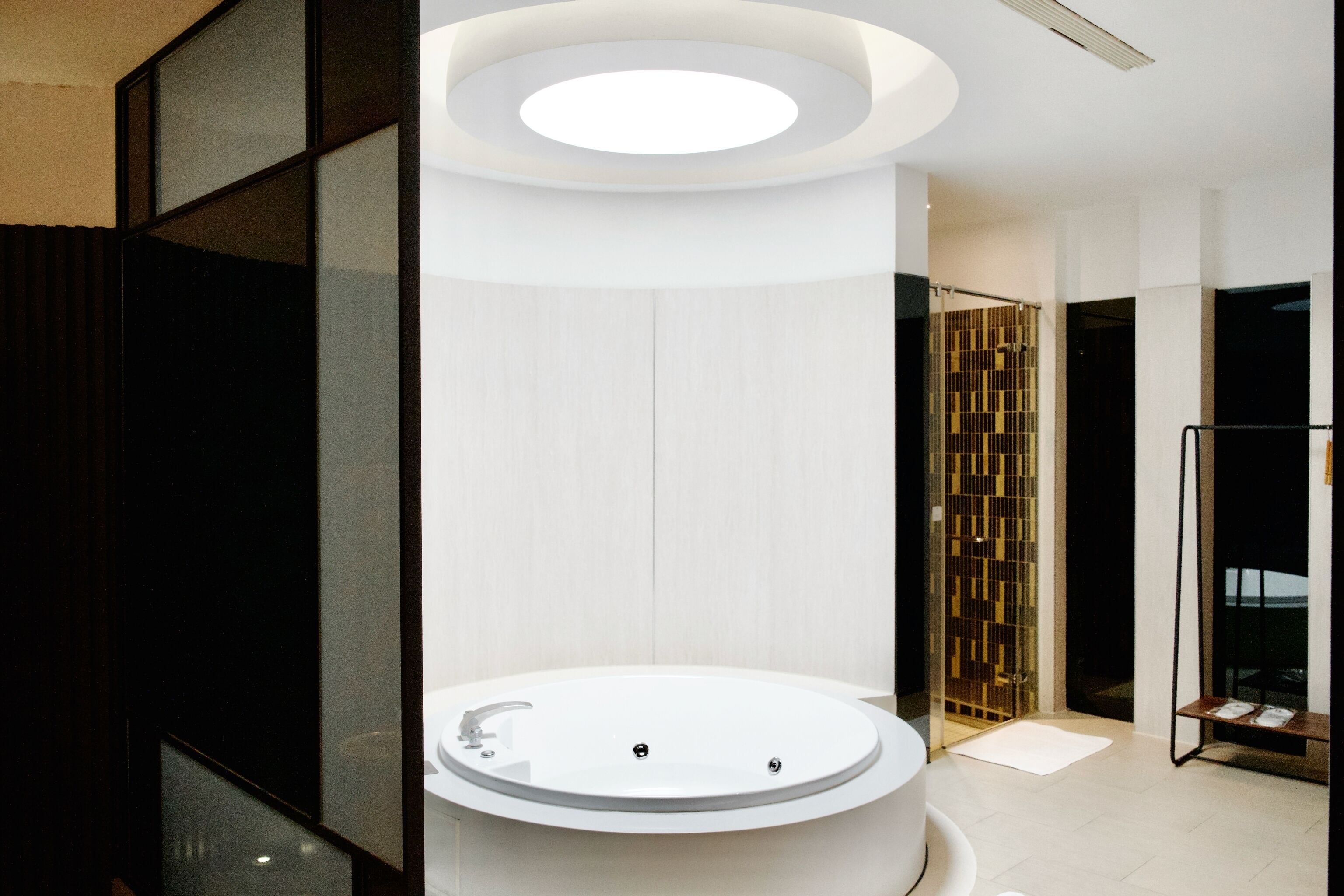 A modern bathroom with a central circular sink, a glass partition, and a wooden panel wall.