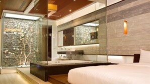 A modern hotel room with a large bed, a glass-enclosed bathroom, and a stone wall with a decorative tree. - H Villa (Tainan)