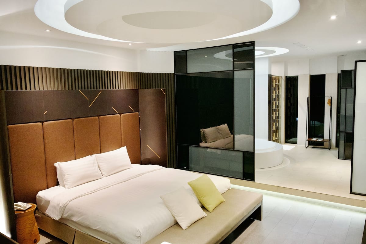 A modern bedroom with a large bed, a headboard with vertical lines, and a glass partition.