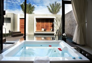Un moderno espacio de spa con hidromasaje, asientos de madera y vistas al exterior.
