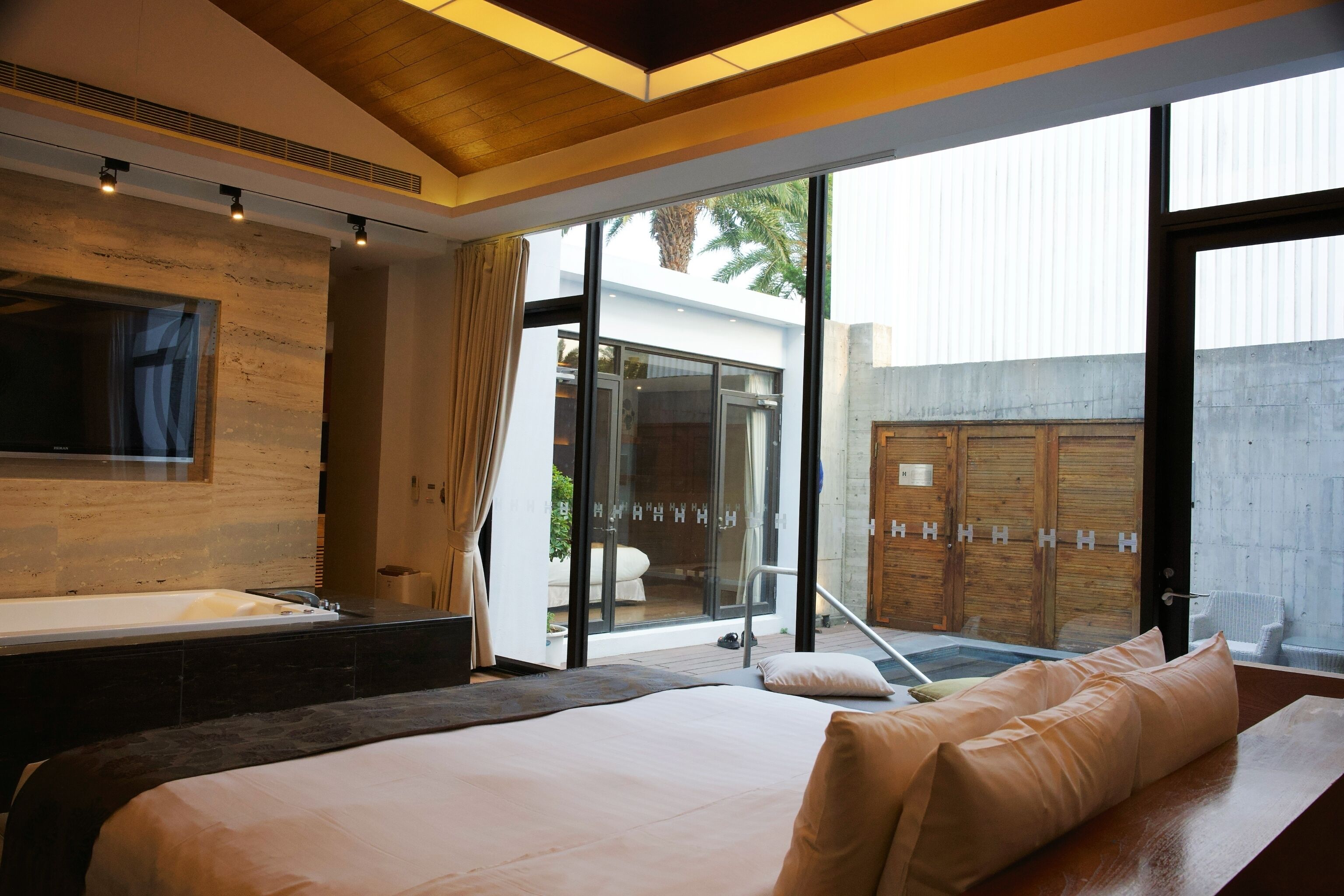 A modern bedroom with a large bed, a bathtub, and a glass door leading to a balcony.