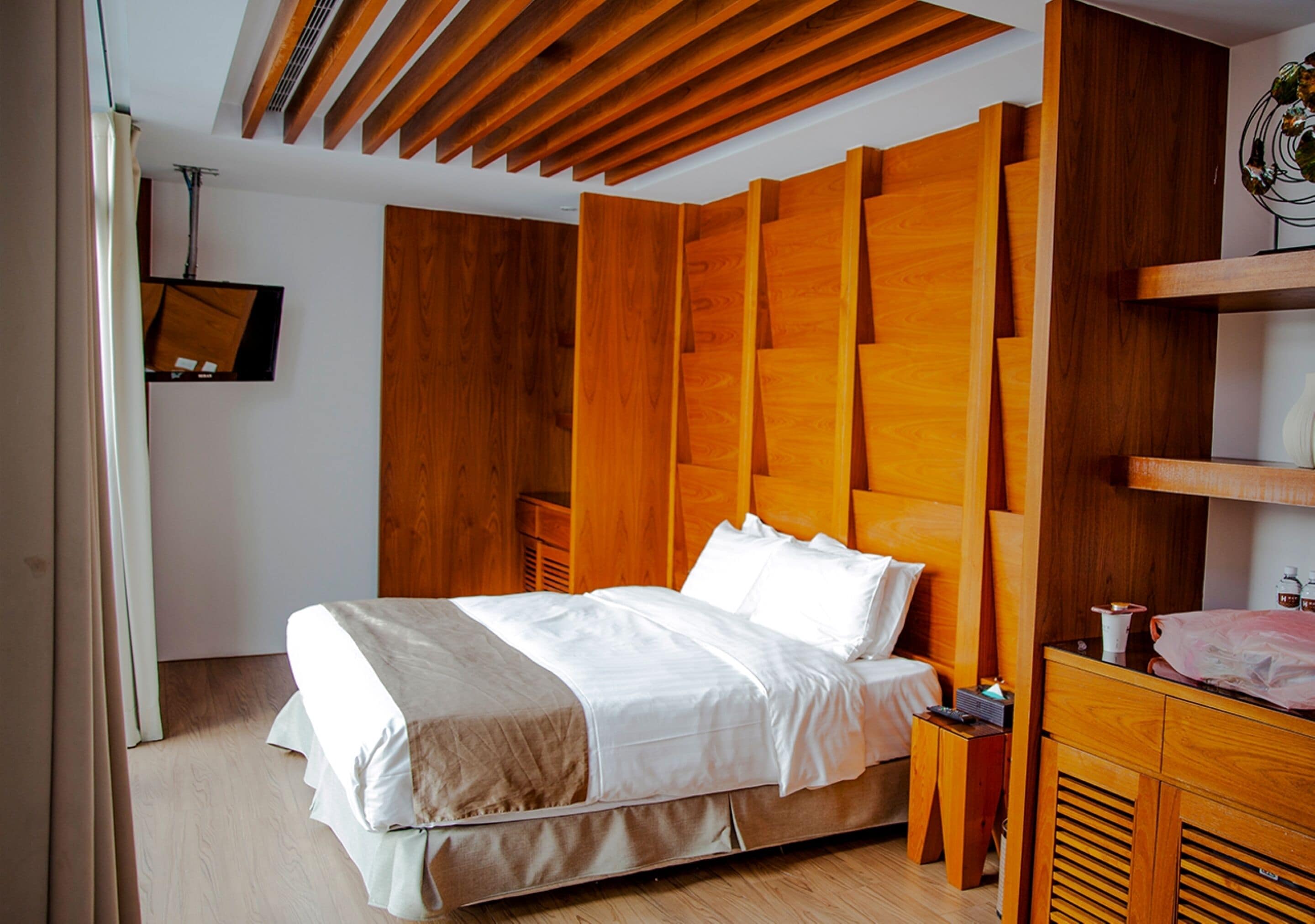 A modern bedroom with a wooden headboard, a bed with white linens, a bedside table, and a wooden dresser.