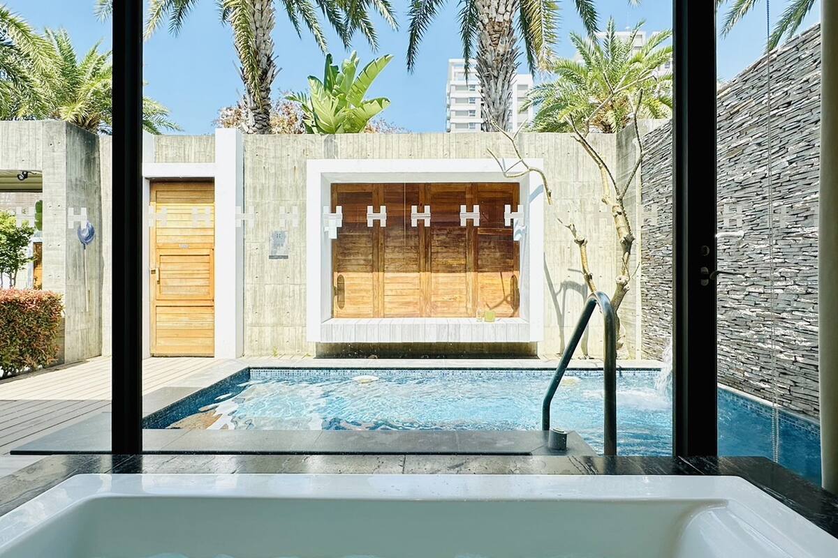 A modern outdoor pool area with a hot tub, a wooden door, and a stone wall.