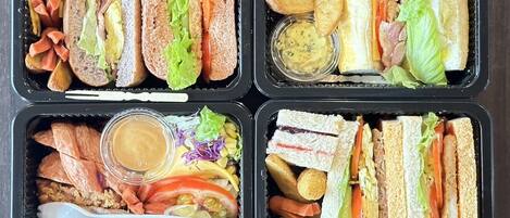 Cuatro recipientes con sándwiches, verduras y salsas.