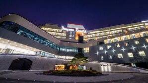 Um hotel moderno com fachada curva, sinalização iluminada e área de entrada ajardinada.