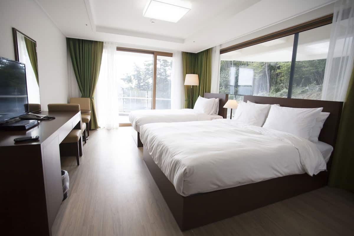 A hotel room with a bed, a desk with a laptop, a chair, and a TV.