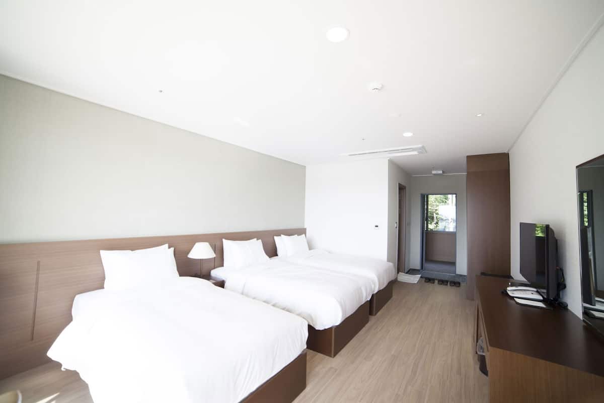 A modern hotel room with two beds, a TV, and a balcony.