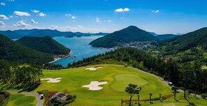 Campo de golf con búnkeres, una masa de agua y un pueblo al fondo.