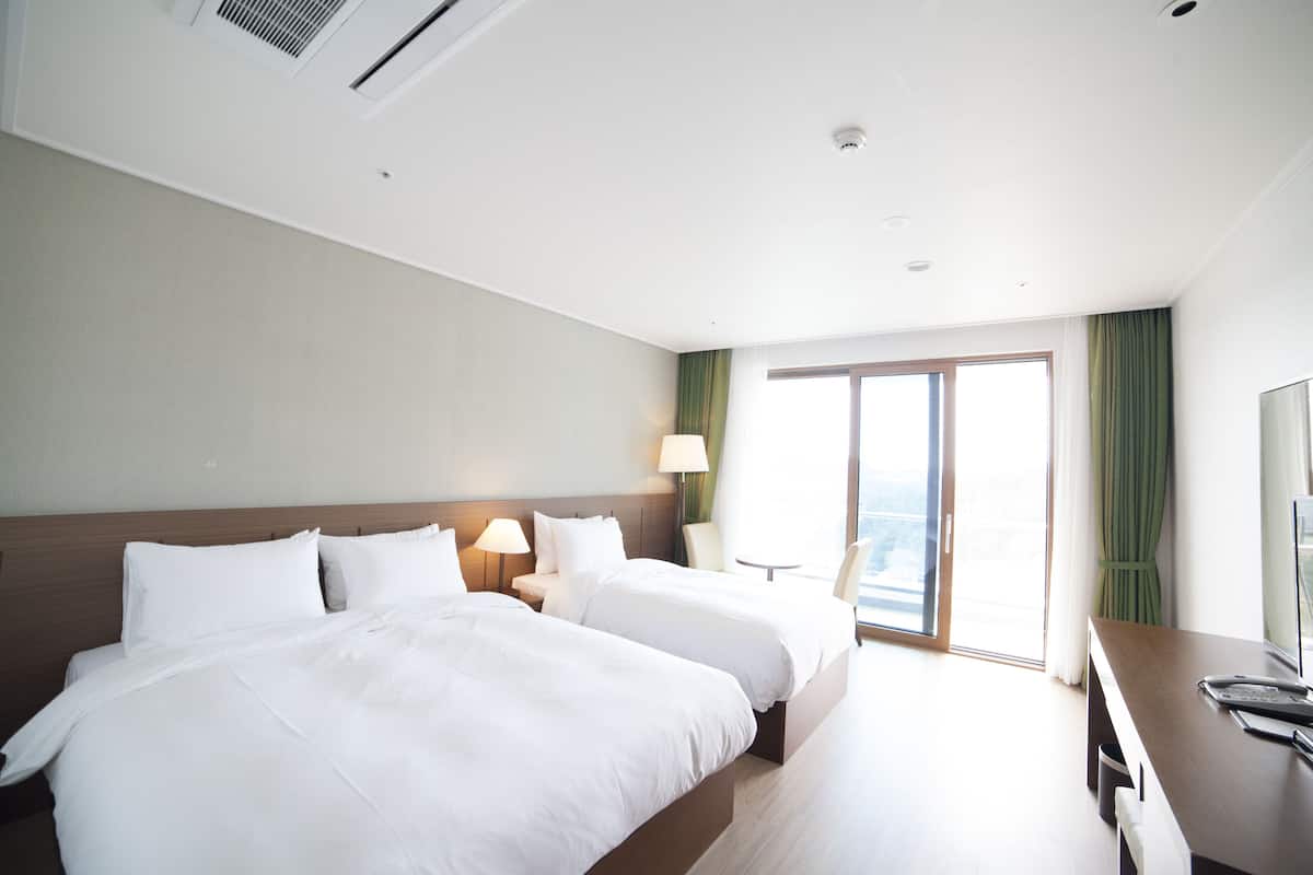 A hotel room with two beds, a desk, a chair, a TV, and a window with curtains.