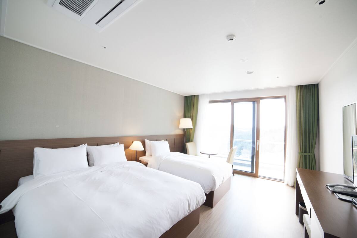 A hotel room with two beds, a desk, a chair, a TV, and a window with curtains.