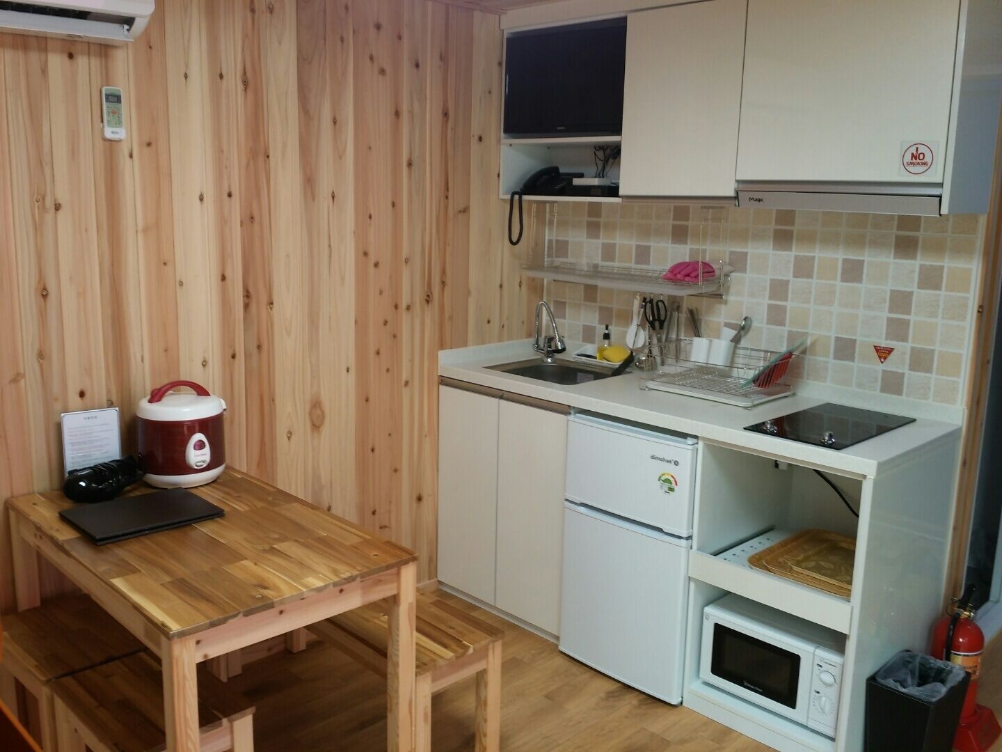 Une cuisine compacte avec une table en bois, un cuiseur à riz, un four à micro-ondes et un petit réfrigérateur.