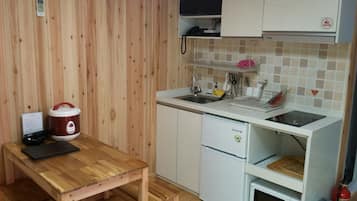 Une cuisine compacte avec une table en bois, un cuiseur à riz, un four à micro-ondes et un petit réfrigérateur.