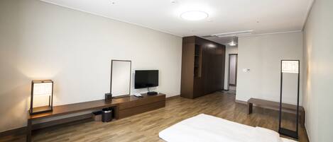 Una habitación de hotel moderna con suelo de madera, televisor de pantalla plana, mesita de noche, una banca y un espejo grande.